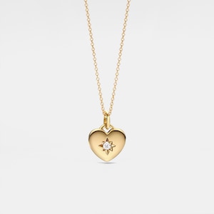 Può includere: Una collana d'oro con un ciondolo a forma di cuore che presenta un piccolo diamante al centro.