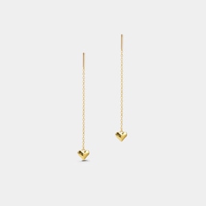 May include: A pair of gold-colored drop earrings. Each earring features a small, heart-shaped charm suspended from a delicate chain. The earrings have a simple, elegant design, with a post at the top.