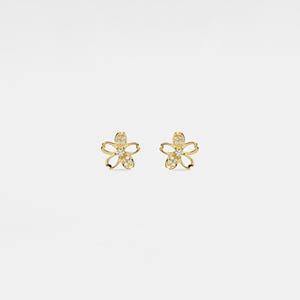 May include: A pair of gold-colored flower-shaped stud earrings. Each earring features five petals and is embellished with small, clear gemstones. The center of each flower is also adorned with gemstones, adding sparkle to the jewelry.