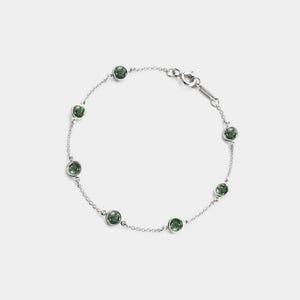 May include: A delicate silver bracelet featuring seven round, dark green gemstones. The bracelet has a fine chain and a secure clasp. The gemstones are evenly spaced along the chain, creating a simple yet elegant design.