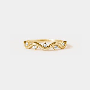 May include: A delicate gold band ring with a wavy design and five small clear gemstones.