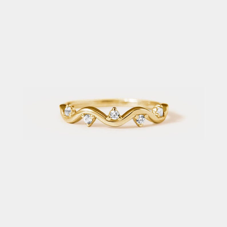 May include: A delicate gold band ring with a wavy design and five small clear gemstones.