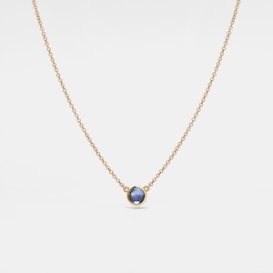 Op de afbeelding: Een delicate gouden ketting met een klein, rond blauw edelsteen hanger.