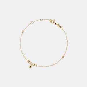 May include: A gold chain bracelet with a small dangling charm and a few small beads along the chain.