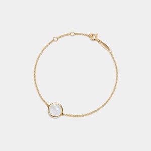 May include: A gold chain bracelet with a white mother-of-pearl circle pendant.