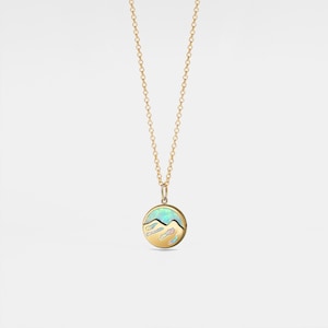 Puede incluir: Un collar de cadena de oro con un colgante redondo que presenta una piedra de ópalo azul y blanca con un diseño de montaña.