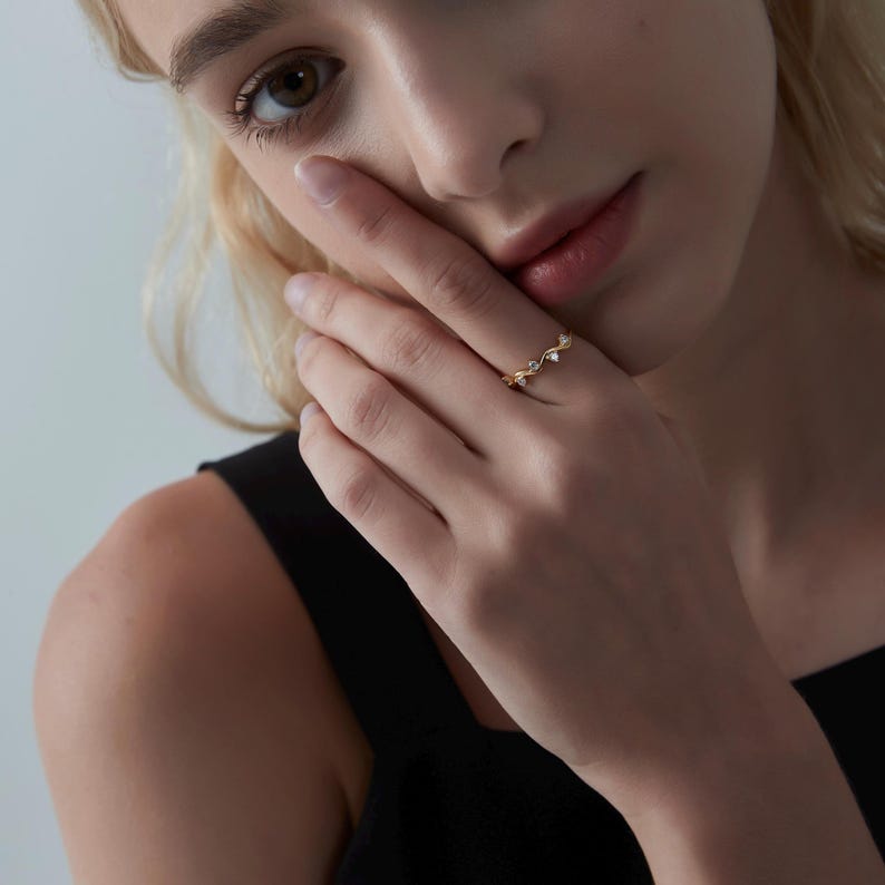 May include: A gold ring with a delicate vine design and small clear stones. The ring is worn on a person's finger.