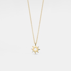 Pode incluir: Um colar de ouro com um pingente de sol. O sol é um design simples com um círculo no centro e raios que se estendem para fora.