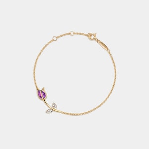 Peut inclure: Un bracelet délicat en chaîne dorée avec un pendentif en forme de rose en pierre précieuse violette. La rose a une seule tige avec deux feuilles qui sont accentuées de petits diamants.
