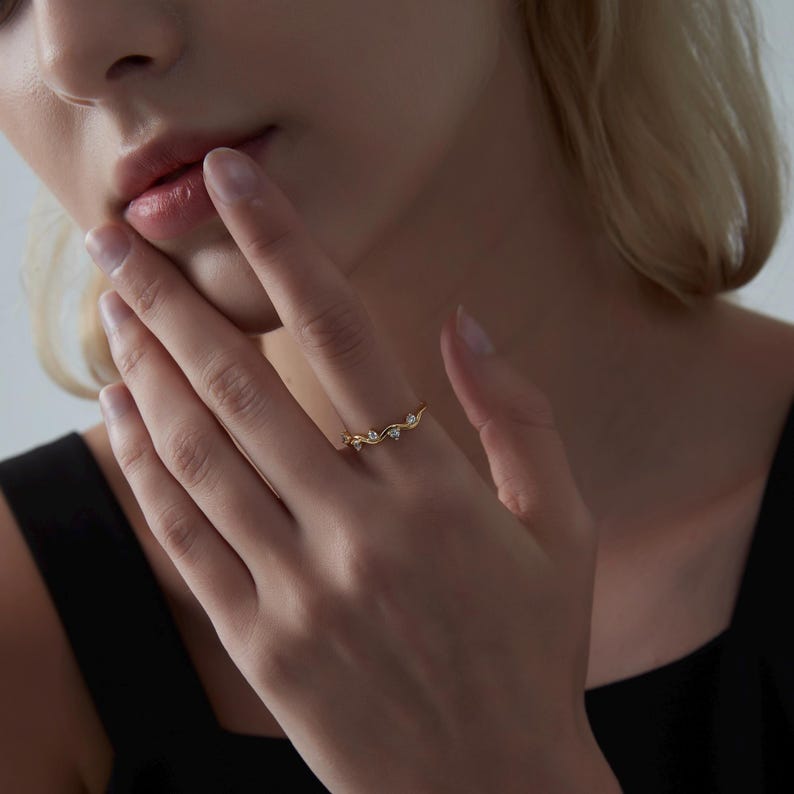 May include: A delicate gold ring with a vine design and small clear stones. The ring is worn on a finger.