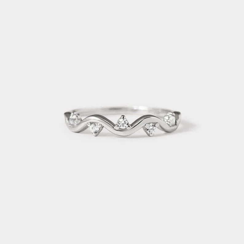 May include: A silver ring with a wavy band and five small clear stones.