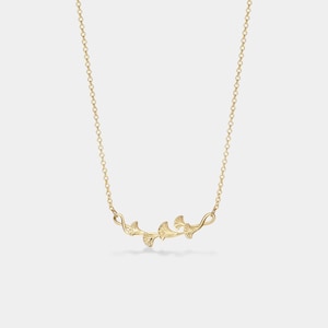 May include: A delicate gold necklace with a pendant featuring a stylized design of ginkgo leaves.