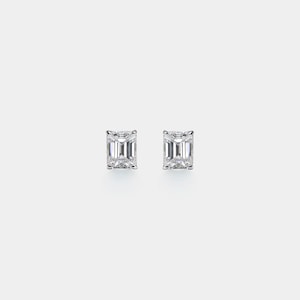 May include: A pair of square emerald-cut diamond stud earrings. The diamonds are set in a silver metal. The earrings are displayed on a white background.