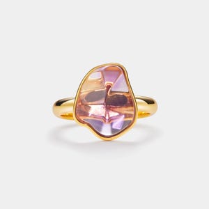 Puede incluir: Un anillo de oro con una gran piedra preciosa de forma irregular, de color púrpura y rosa.