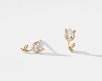 May include: A pair of gold-toned earrings featuring a delicate tulip design with a clear crystal stone in the center.
