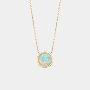 May include: A gold-toned necklace featuring a round pendant with an opal center and a halo of small, clear stones. The opal displays a range of colors, including blue, green, and white. The chain is delicate and appears to be gold.