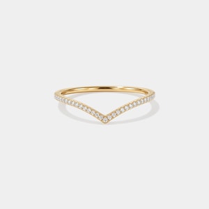 May include: A gold-colored V-shaped ring with a band of small, clear gemstones. The ring has a delicate design and is set against a white background. The ring is a piece of jewelry.
