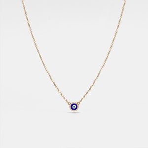 Könnte beinhalten: Eine goldene Kettenkette mit einem kleinen blauen Glücksbringer in Form eines bösen Auges. Der Anhänger hat eine weiße Mitte.