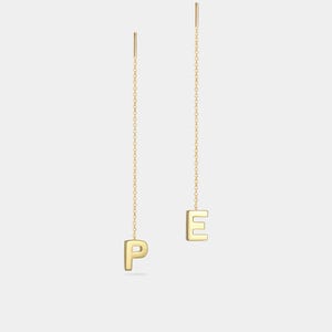 May include: Gold-colored dangle earrings spelling out the letters "PE". The earrings feature a delicate chain design with the letters suspended at the bottom. The letters are in a sans-serif font.
