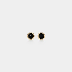 May include: A pair of stud earrings with a round, glossy black stone set in a gold-coloured bezel. The earrings are presented against a plain white background, emphasising their simple elegance and classic design.
