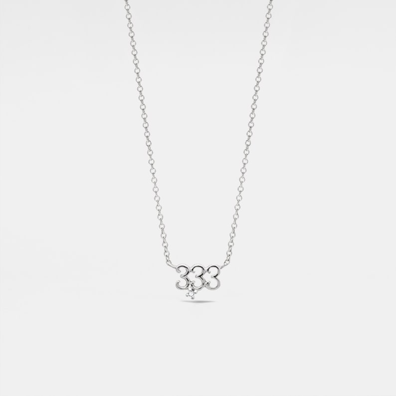 May include: A silver necklace with a pendant featuring the number 333 with a small diamond accent.