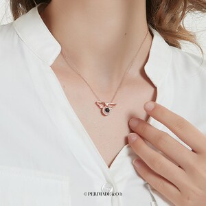 May include: A rose gold necklace with a small angel wing pendant featuring a black stone in the center. The pendant has a small halo of clear stones around the black stone.