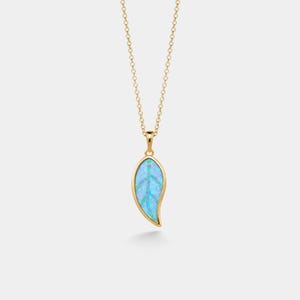 May include: A gold necklace featuring a leaf-shaped pendant with a vibrant blue opal inlay. The pendant is suspended from a delicate gold chain, showcasing a smooth metallic border that frames the iridescent blue stone with a central vein detail.