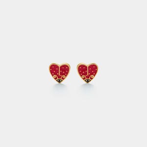 Peut inclure: Une paire de boucles d'oreilles à clous en forme de cœur. Chaque boucle d'oreille présente un motif en émail rouge avec de petits points blancs, ressemblant à une coccinelle. Les boucles d'oreilles ont un bord doré et des accents noirs.