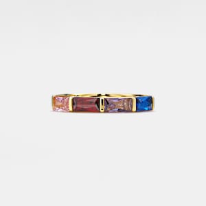 Może przedstawiać: Złoty pierścionek z pięcioma prostokątnymi kamieniami szlachetnymi. Kamienie szlachetne są różowe, czerwone, fioletowe i niebieskie.