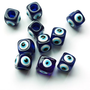 May include: A group of ten blue glass beads with white and black evil eye charms. The beads are square shaped and have a hole in the centre for stringing.