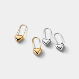 May include: Four heart-shaped earrings in gold and silver tones. The earrings have a safety pin design, with a curved top and a heart-shaped bottom. The earrings are displayed on a white background.