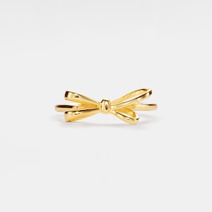 Puede incluir: Un anillo de color dorado con un diseño de lazo.