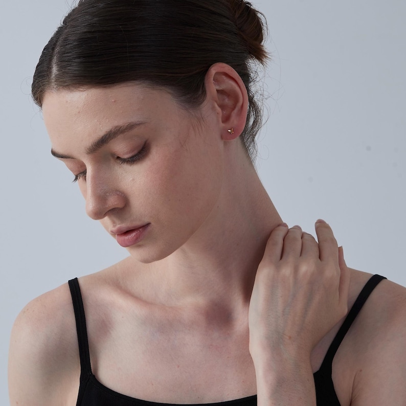 K&ouml;nnte beinhalten: Nahaufnahme eines Ohrs mit einem kleinen goldenen Ohrstecker. Die Person tr&auml;gt ein schwarzes Tanktop.