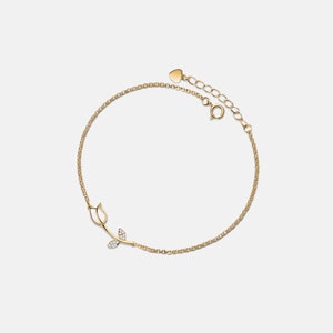 May include: A delicate gold chain bracelet with a small rose design featuring clear cubic zirconia stones. The bracelet has a heart-shaped lobster clasp.