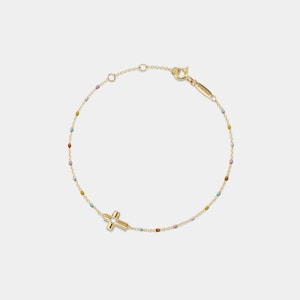 May include: A gold bracelet with a cross pendant and a small, clear gemstone. The chain is decorated with small, colourful beads. The bracelet's clasp is also gold-coloured.