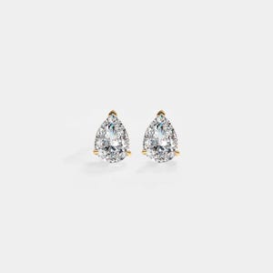 Op de afbeelding: Een paar peervormige diamanten oorstekers. Elke oorbel heeft een heldere, facetgeslepen diamant gezet in een gouden prong setting. De diamanten worden gepresenteerd tegen een witte achtergrond.