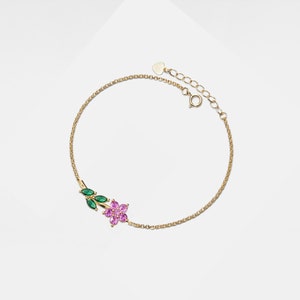 May include: A gold chain bracelet with a pink flower and green leaves charm. The bracelet has a heart-shaped clasp.
