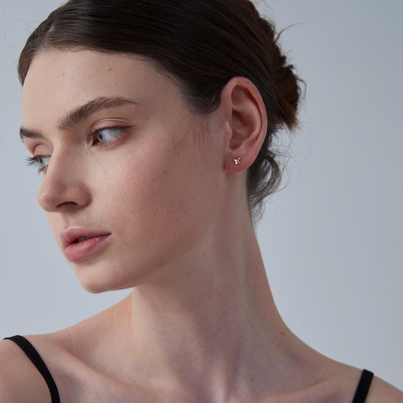 K&ouml;nnte beinhalten: Nahaufnahme eines Ohrs mit einem kleinen goldenen Ohrstecker. Der Ohrstecker ist schlicht gehalten und hat eine kleine, runde Form.