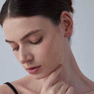 K&ouml;nnte beinhalten: Nahaufnahme eines Ohrs mit einem kleinen goldenen Ohrstecker. Der Ohrstecker ist in einem einfachen, runden Design gehalten.