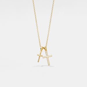 Puede incluir: Un collar de cadena de oro con dos colgantes en forma de cruz. Una cruz es de oro liso, y la otra está engastada con pequeños diamantes.