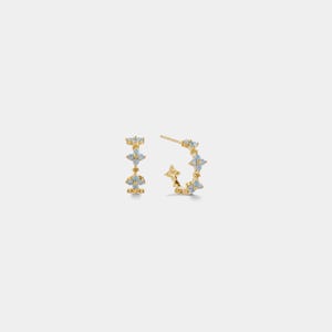 May include: A pair of gold-coloured hoop earrings and a matching stud earring. Each earring features light blue gemstone accents in a floral pattern. The earrings are set against a white background.