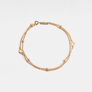 May include: A gold chain bracelet with two strands and small heart charms. The bracelet has a clasp closure.