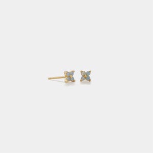 May include: A pair of gold stud earrings, each featuring a four-petal flower design. The petals are a light blue color, and the earrings are set against a white background.