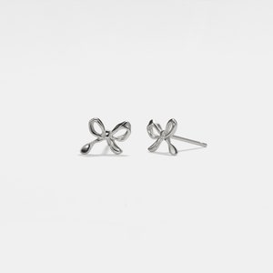 May include: A pair of silver bow-shaped stud earrings.