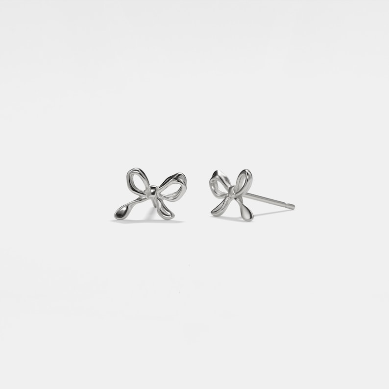 May include: A pair of silver bow-shaped stud earrings.