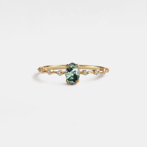 May include: A gold ring featuring an oval-shaped green moss agate gemstone. The ring has a delicate band with small, clear accent stones. The design is elegant and suitable for everyday wear or special occasions.