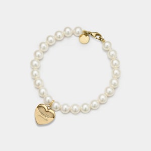 Puede incluir: Un brazalete de perlas doradas con un dije en forma de corazón que dice "Te amo".