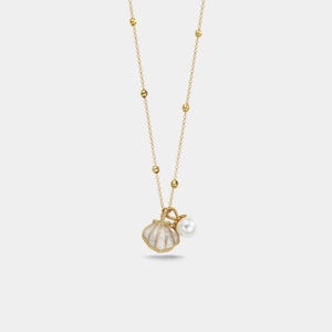 Könnte beinhalten: Eine goldfarbene Halskette mit einem Muschel-Anhänger und einer Perle. Der Anhänger hat ein weißes und goldenes Design, und die Kette hat kleine goldene Perlen. Die Perle ist weiß und rund.