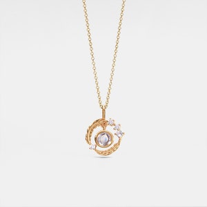 May include: Gold necklace with a moonstone pendant surrounded by a circle of leaves and small diamonds.