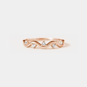 May include: A rose gold band ring with a wavy design and five small clear gemstones.